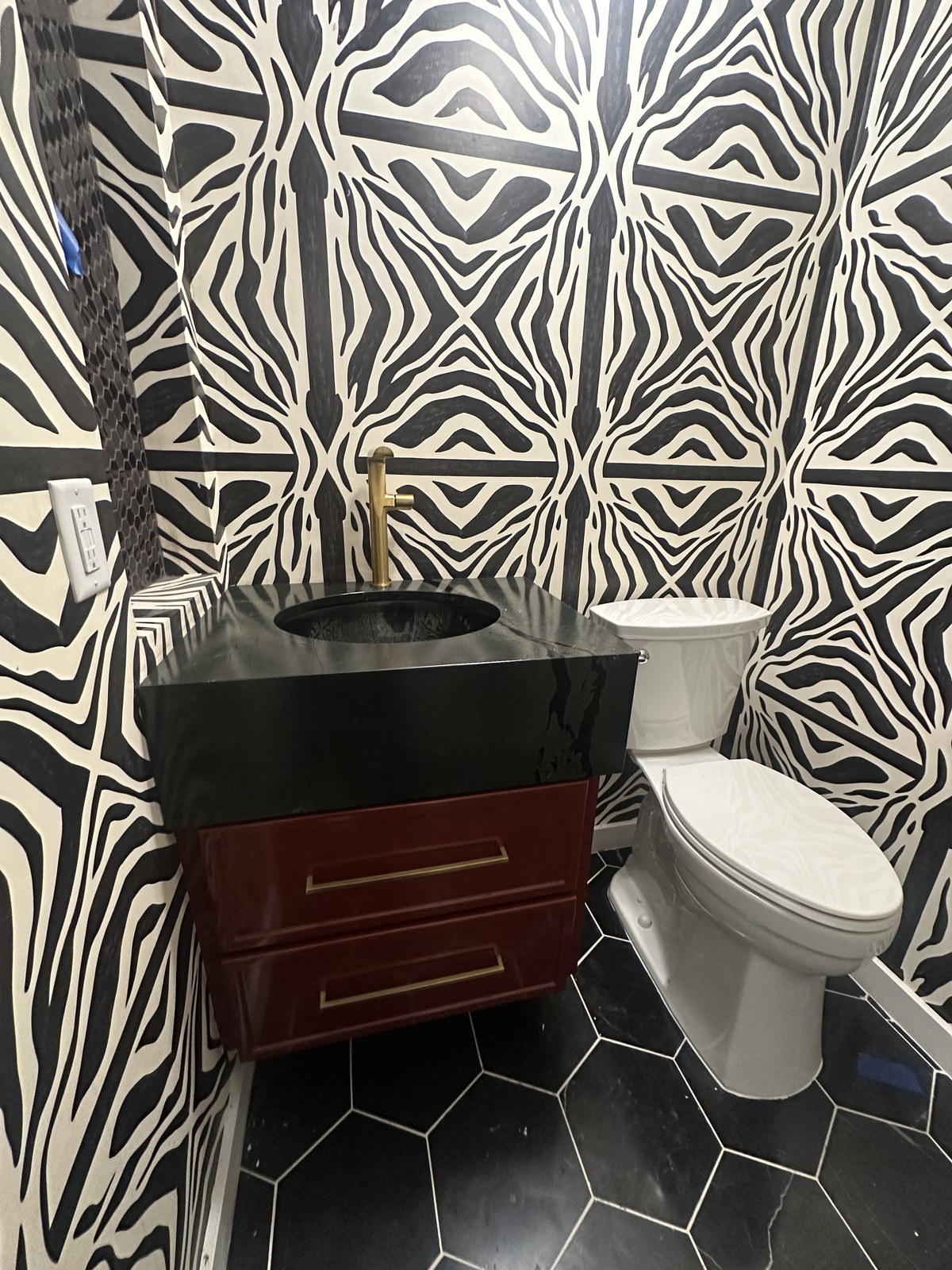Powder room by Haven Renovations — bold graphic wallpaper with a red lacquer vanity and black stone top