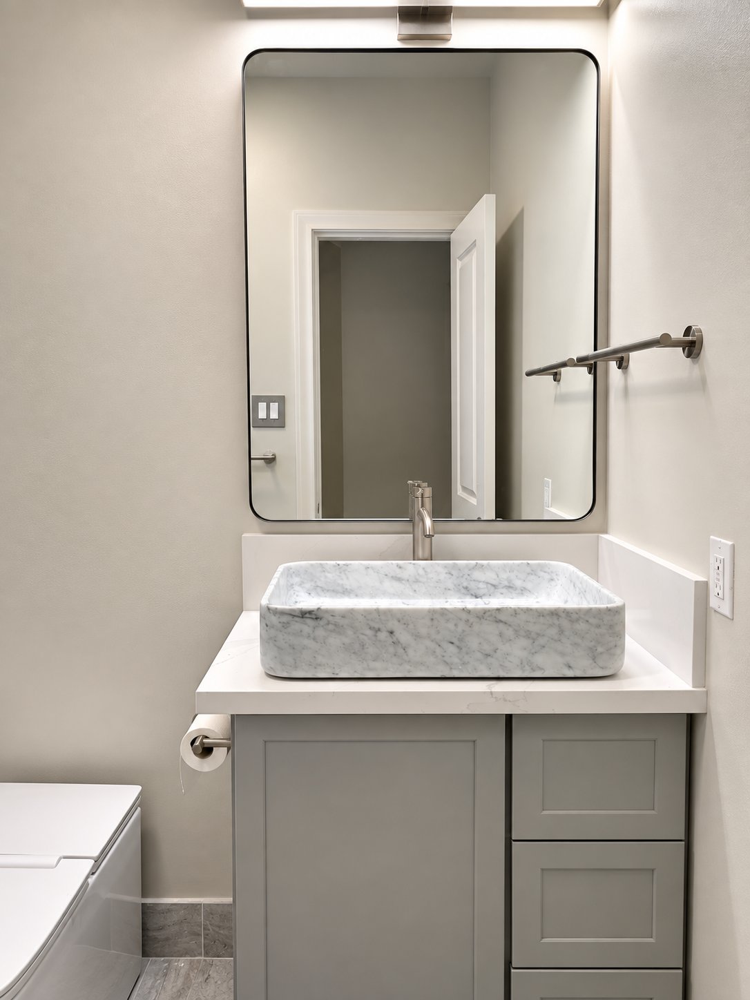 Marble vessel sink on a gray vanity beneath a rectangular mirror